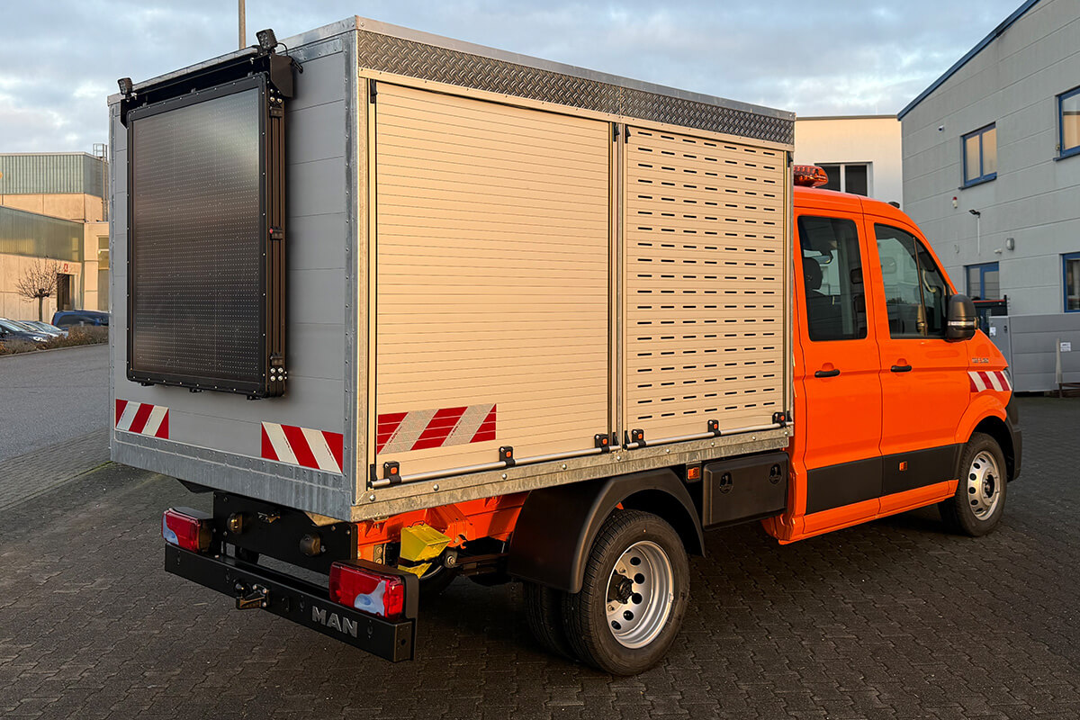 Orangefarbener Transporter mit Kofferaufbau und LED-Warntafel am Heck.